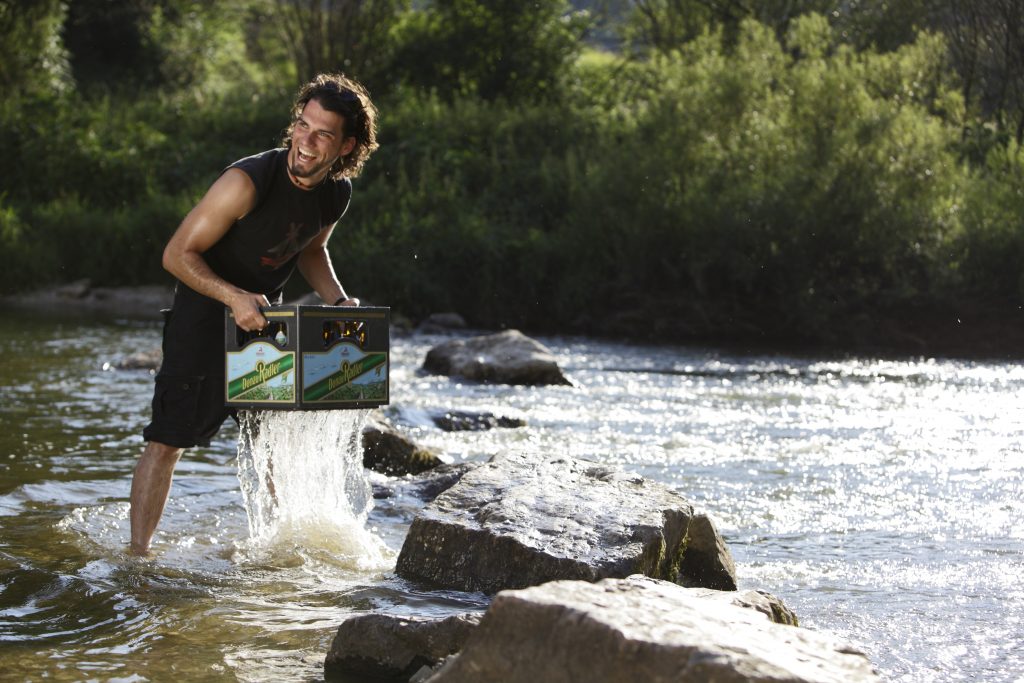Mann im Anzug steht im Wasser und hält eine Kiste Bier.