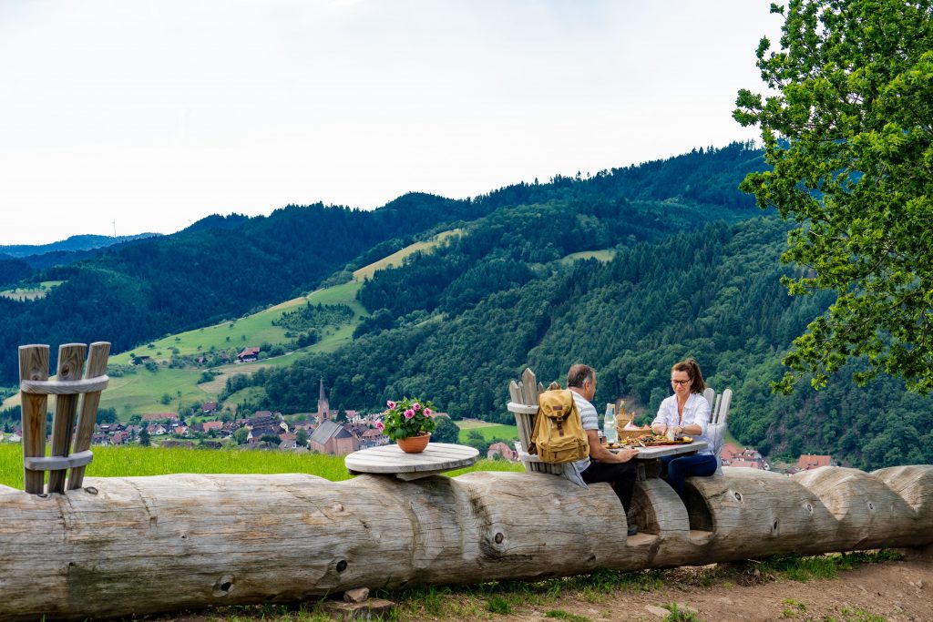 Die lange Baumstamm-Bank am Schwarzwälder Genießerpfad „Harmersbacher Vesperweg“ in Oberharmersbach. Im „Donissi Hofladen“ von Markus Schwarz lässt sich der Rucksack mit regionalen Spezialitäten füllen – fürs Picknick auf der Tour.