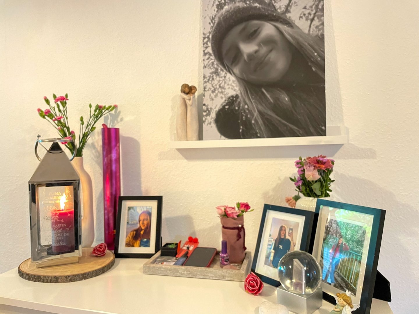"Wir hör'n uns, wenn ich tot bin! - Trauer und KI": Vor einer weißen Wand ist ein Gedenkschrein für die verstorbene Tochter mit Fotos, Blumen und einer Kerze aufgebaut.