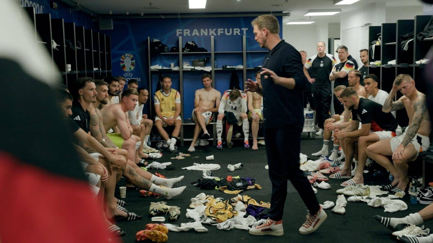 Emotionale Ansprache in der Kabine: Der Trainer der deutschen Nationalmannschaft spricht zu seinem Team nach einem Spiel bei der Heim-EM 2024 in Frankfurt. Spieler hören aufmerksam zu, während die Kabine von der Intensität des Moments geprägt ist.