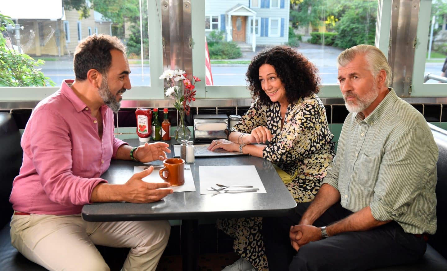 "Das Traumschiff: Hudson Valley": Im Diner: An einem Tisch sitzen sich Hanna Liebhold (Barbara Wussow) und Thomas Wellenstein (Adnan Maral) gegenüber und unterhalten sich angeregt. Neben Hanna sitzt Martin Grimm (Daniel Morgenroth), seinen Blick nachdenklich von den beiden abgewendet.