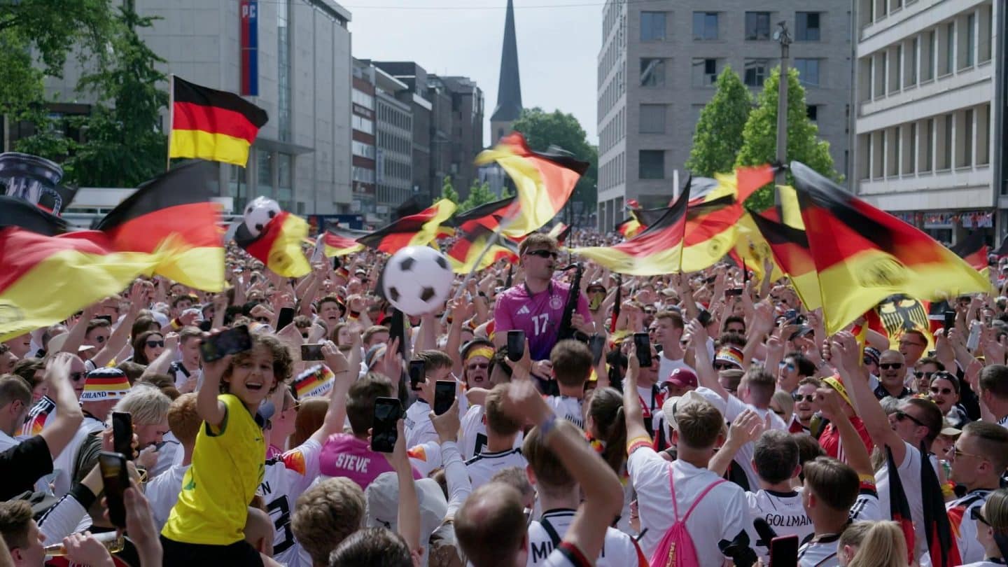 Jubelnde Menschenmenge in Deutschland während der EM 2024: Fans in schwarz-rot-goldener Kleidung schwenken Fahnen und feiern auf den Straßen, die Atmosphäre voller Euphorie und Gemeinschaftsgefühl.