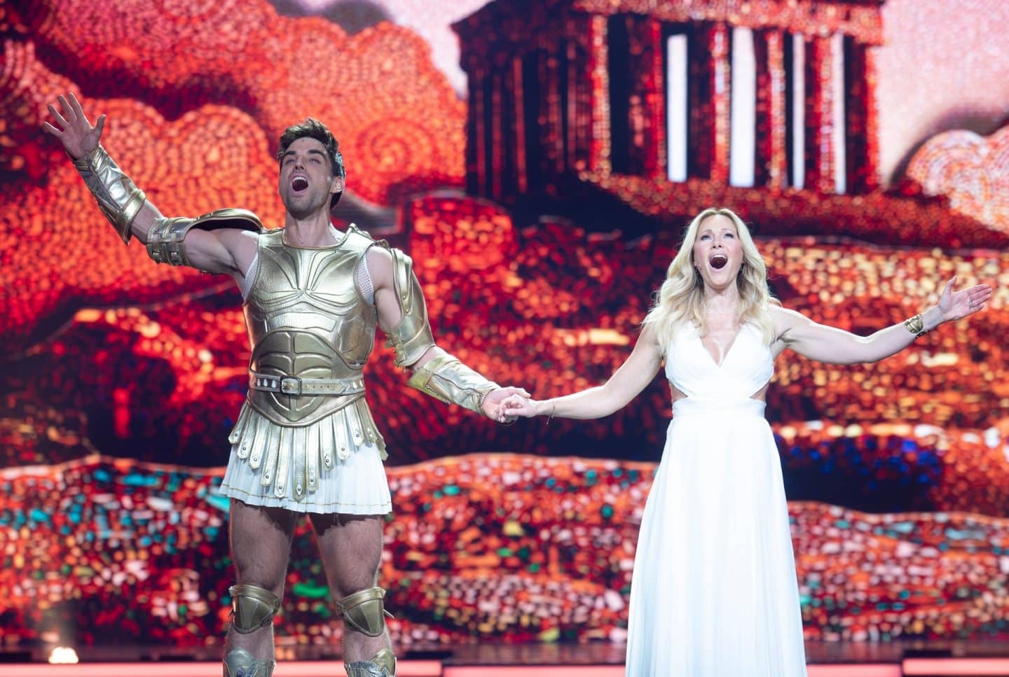 ldbeschreibung:
"Die Helene Fischer-Show": Herkules Darsteller Philipp Büttner und Helene Fischer stehen singend auf der Bühne. Beide sind in einer totalen Kameraeinstellung zu sehen. Sie halten sich an der Hand und stehen frontal zur Kamera. Philipp Büttner trägt als Herkules typisch, einen goldenen Brustpanzer mit weißem Rock und goldenen Stiefeln. Helene Fischer in einem weißen, bodenlangen Kleid. Im Hintergrund-Content die Akropolis.