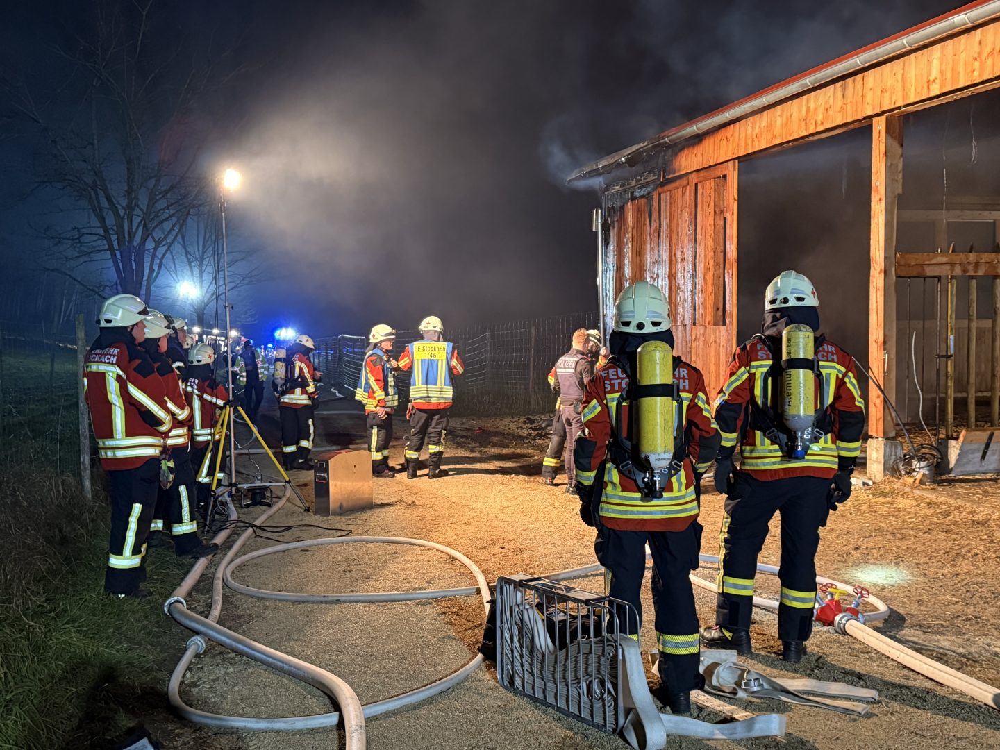 Feuerwehrkräfte in Schutzkleidung bekämpfen einen Stallbrand in Stockach-Airach. Die Einsatzstelle ist mit Schlauchleitungen und Beleuchtung ausgerüstet.