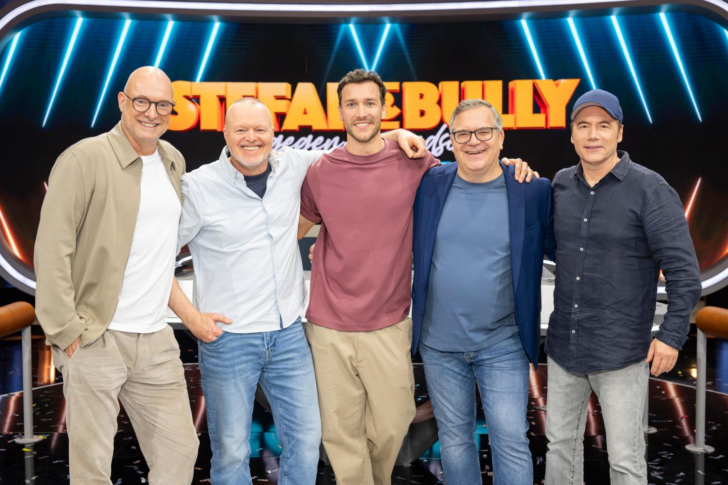 Gruppenfoto der Show 'Stefan & Bully gegen irgendson Schnulli': Frank Buschmann, Stefan Raab, Kandidat Marc, Moderator Elton und Michael 'Bully' Herbig stehen lächelnd vor dem leuchtenden Show-Logo auf der Bühne.