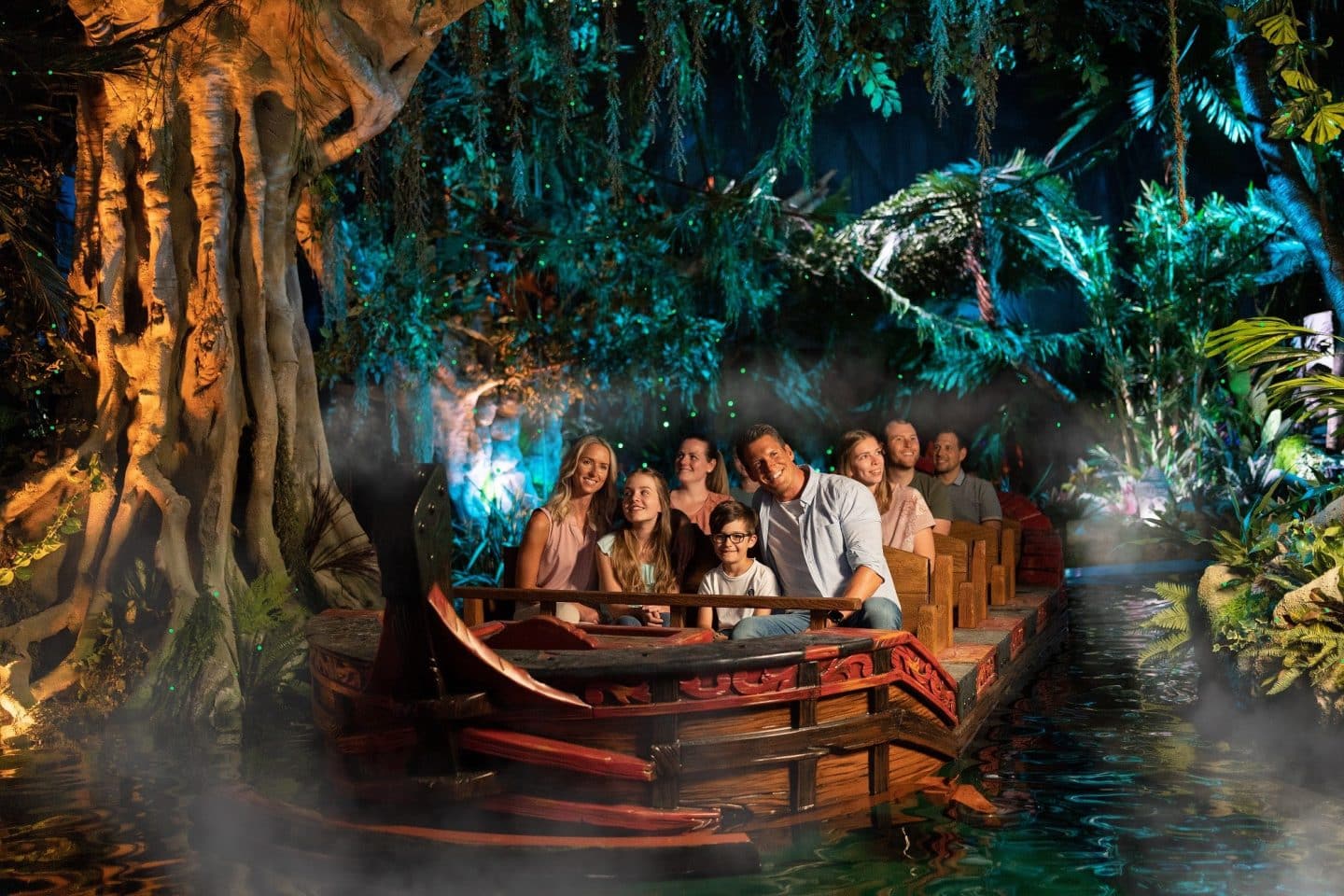 Eine Familie und weitere Besucher sitzen in einem Boot der Attraktion „Piraten in Batavia“ im Europa-Park. Sie fahren durch eine tropische Szenerie mit üppigem Pflanzenbewuchs, stimmungsvoller Beleuchtung und einem großen, verwunschenen Baum im Hintergrund.






