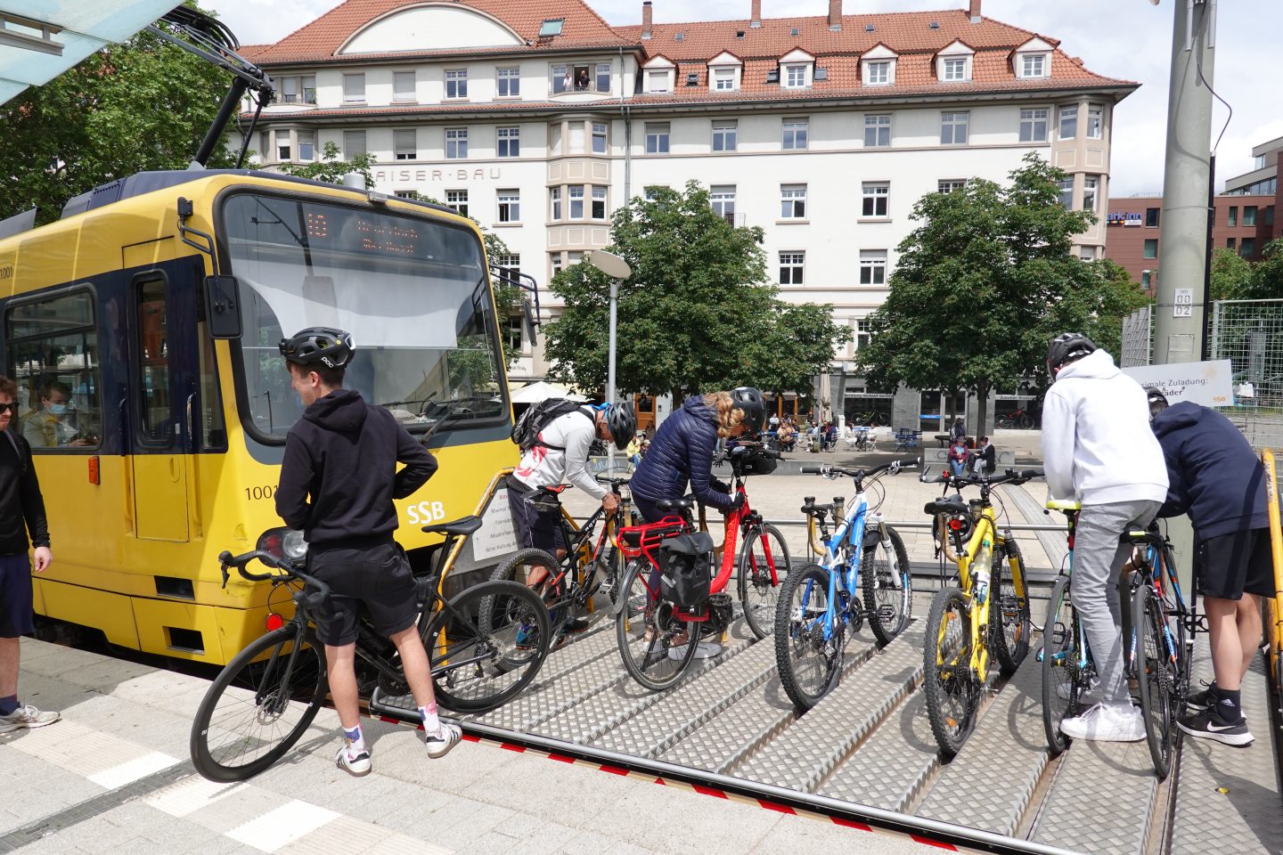 Eine Gruppe von Radfahrern belädt den Fahrrad-Vorstellwagen der Stuttgarter Zahnradbahn am Marienplatz. Im Hintergrund ist die gelbe Zahnradbahn zu sehen, die als Symbol für Stuttgarts steilen Nahverkehr gilt.






