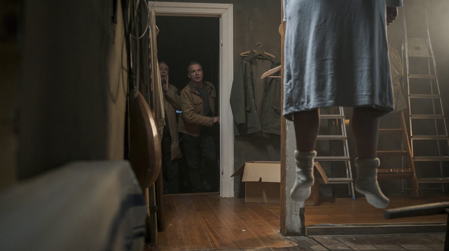 Lars Nolden (gespielt von Dirk Böhling) und Hauke Jacobs (gespielt von Hinnerk Schönemann) betreten vorsichtig den Dachboden und machen eine schockierende Entdeckung: Eine Person, gehüllt in einen Bademantel und Wollsocken, hängt leblos von der Decke. Die Szene ist düster und von einem unheimlichen Licht durchzogen, was die beklemmende Atmosphäre verstärkt.