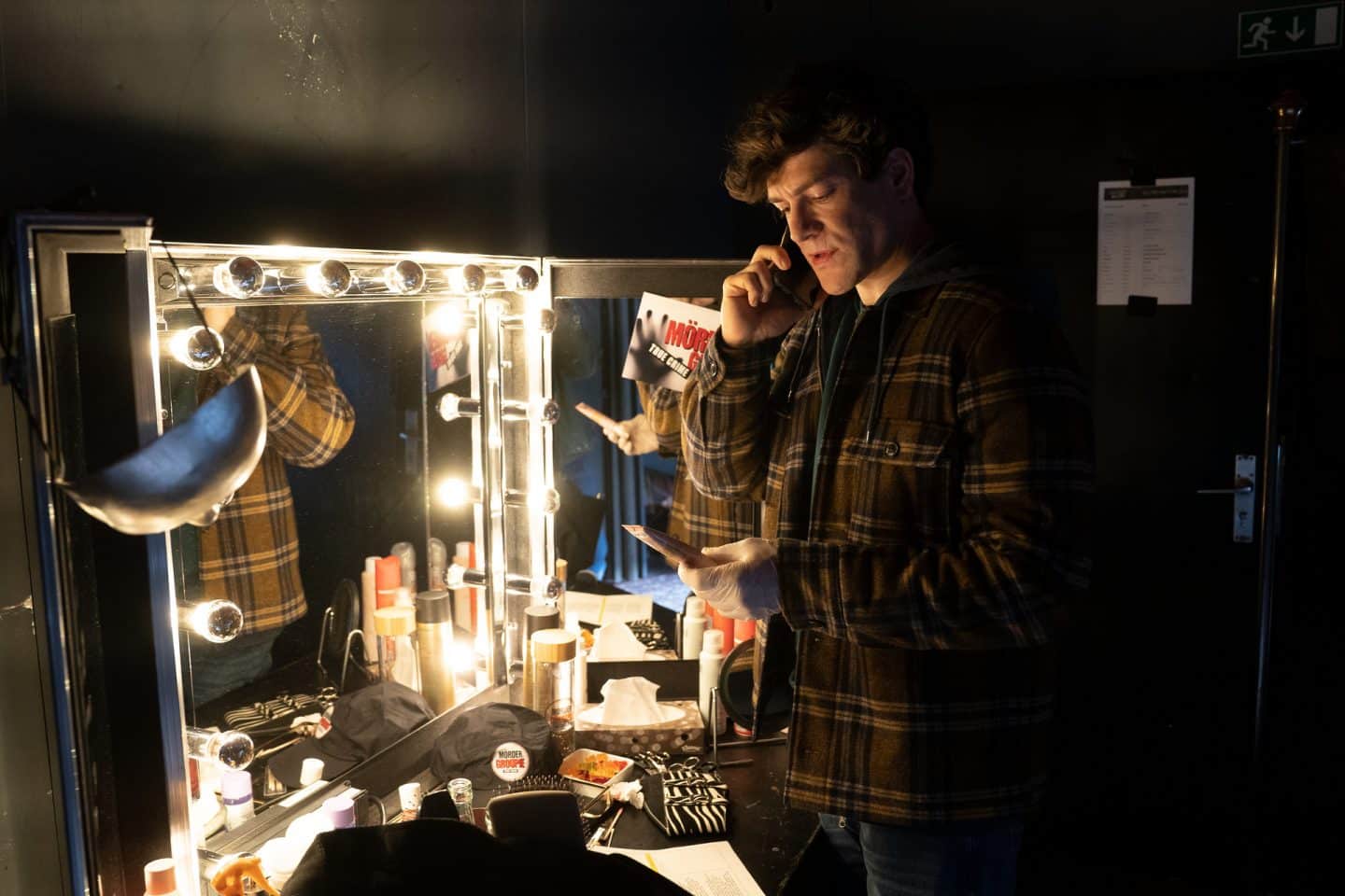 "Die Chefin - True Crime": Telefonierend steht Korbinian Kirchner (Jonathan Hutter) vor einem mit etlichen Glühbirnen angestrahlten Aufklappspiegel und betrachtet eine Tube in seiner Hand.
