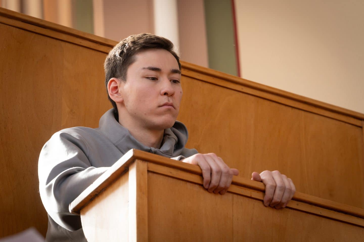 "Wilsberg - Über dem Gesetz": Jan Seiters (David Pimshteyn) sitzt an einer holzvertäfelten Bank in einem Hörsaal und hört konzentriert zu.
