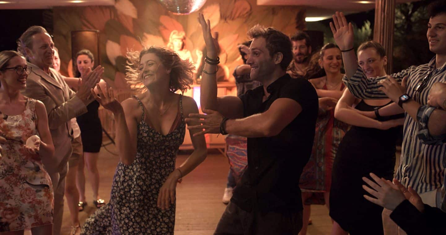 "Ein Sommer in Italien": Billie (Hanna Plaß) und Mateo (Valmir Krasniqi) tanzen den Macarena-Tanz ausgelassen im Beachclub. Sie sind umgeben von mittanzenden Gästen (Komparsen).