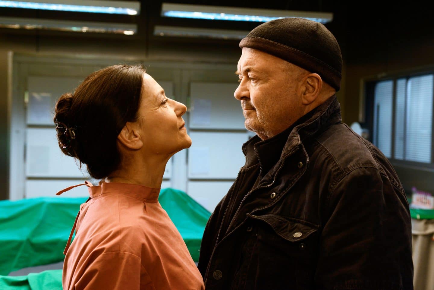 "Ein starkes Team - Der tote Mörder": Otto (Florian Martens) und Dr. Simkeit (Eva Sixt) stehen sich in der Rechtsmedizin gegenüber und lächeln sich herausfordernd an. Im Hintergrund liegt eine zugedeckte Leiche auf dem Obduktionstisch.
