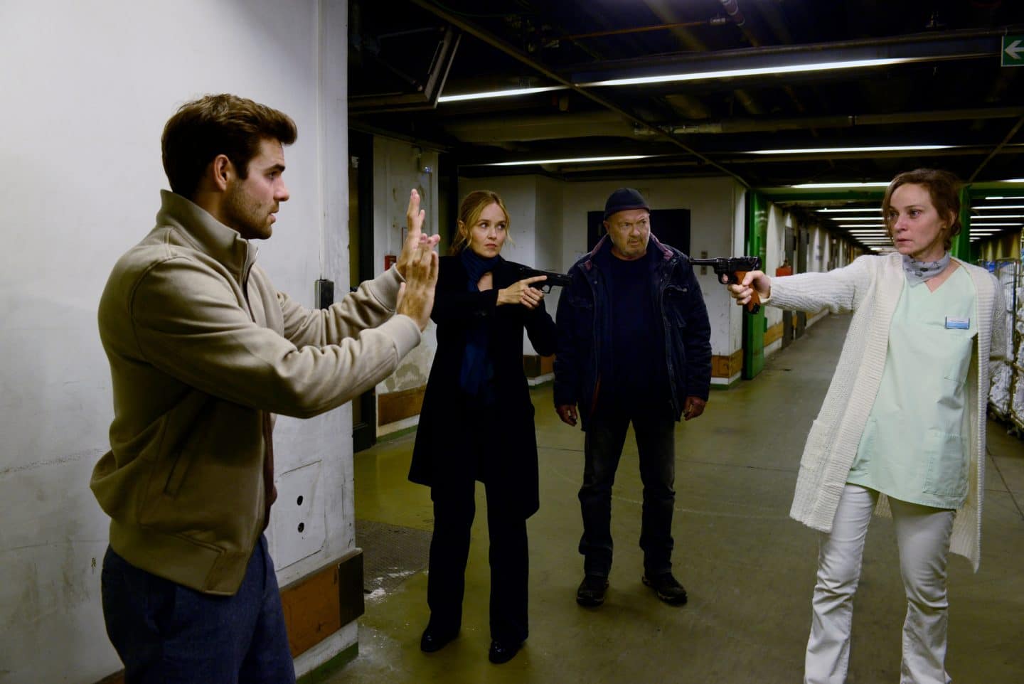 "Ein starkes Team - Der tote Mörder": Marie Lehmann (Jeanette Hain) steht in einem dunklen Kellergang und hat eine Pistole auf Nils Makowski (Lucas Reiber) gerichtet, der mit erhobenen Händen da steht. Linett (Stefanie Stappenbeck) steht ein paar Schritte entfernt zwischen ihnen und hat ihre eigene Waffe auf Marie gerichtet. Neben ihr befindet sich Otto (Florian Martens), der Marie im Blick hält.
