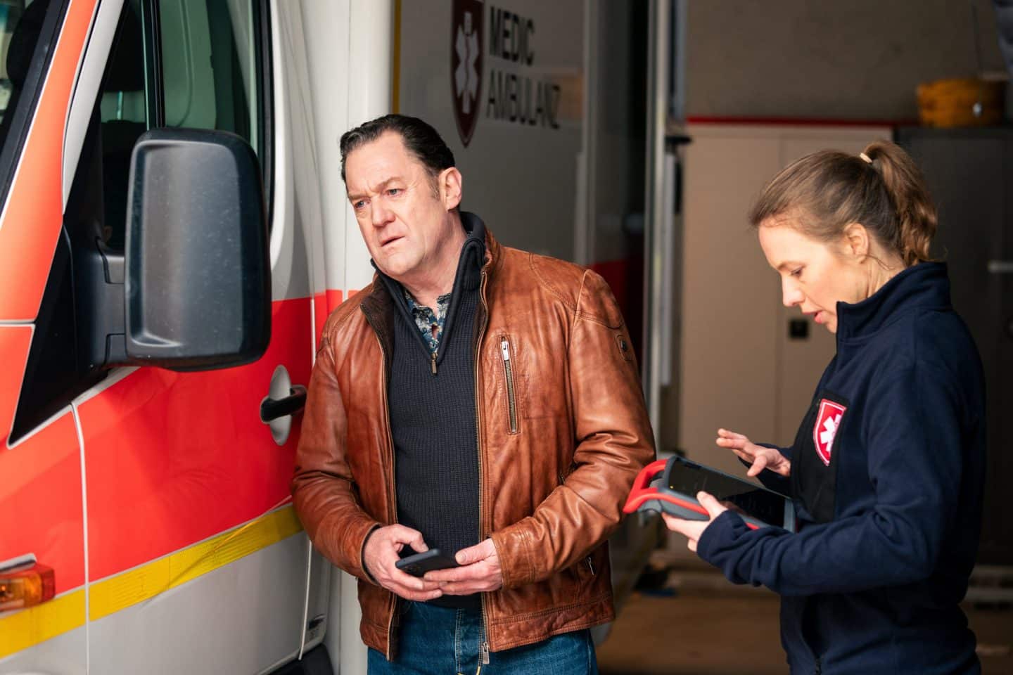 "Die Chefin - Grenzgänger": Paul Böhmer (Jürgen Tonkel) untersucht einen Schaden am Rückspiegel des Rettungswagens. Martina Jessing (Anna Brüggemann) steht neben ihm und prüft auf einem Tablet die Dokumentation.