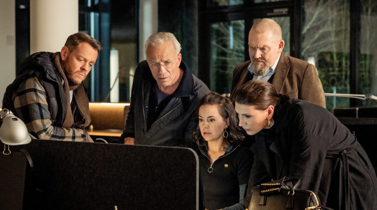 Die Kommissare Norbert Jütte (Roland Riebeling), Max Ballauf (Klaus J. Behrendt) und Freddy Schenk (Dietmar Bär) stehen zusammen mit den Correct Inkasso-Managerinnen Silja Mayer (Karolina Horster) und Milena Ilic (Olga Prokot) vor einem Computerbildschirm. Alle blicken konzentriert auf die Daten, um Hinweise auf den brutalen Überfall auf den Mitarbeiter Fabian Pavlou zu finden. Die Szene zeigt die Ermittlungsarbeit und die Zusammenarbeit zwischen Polizei und Inkasso-Firma.