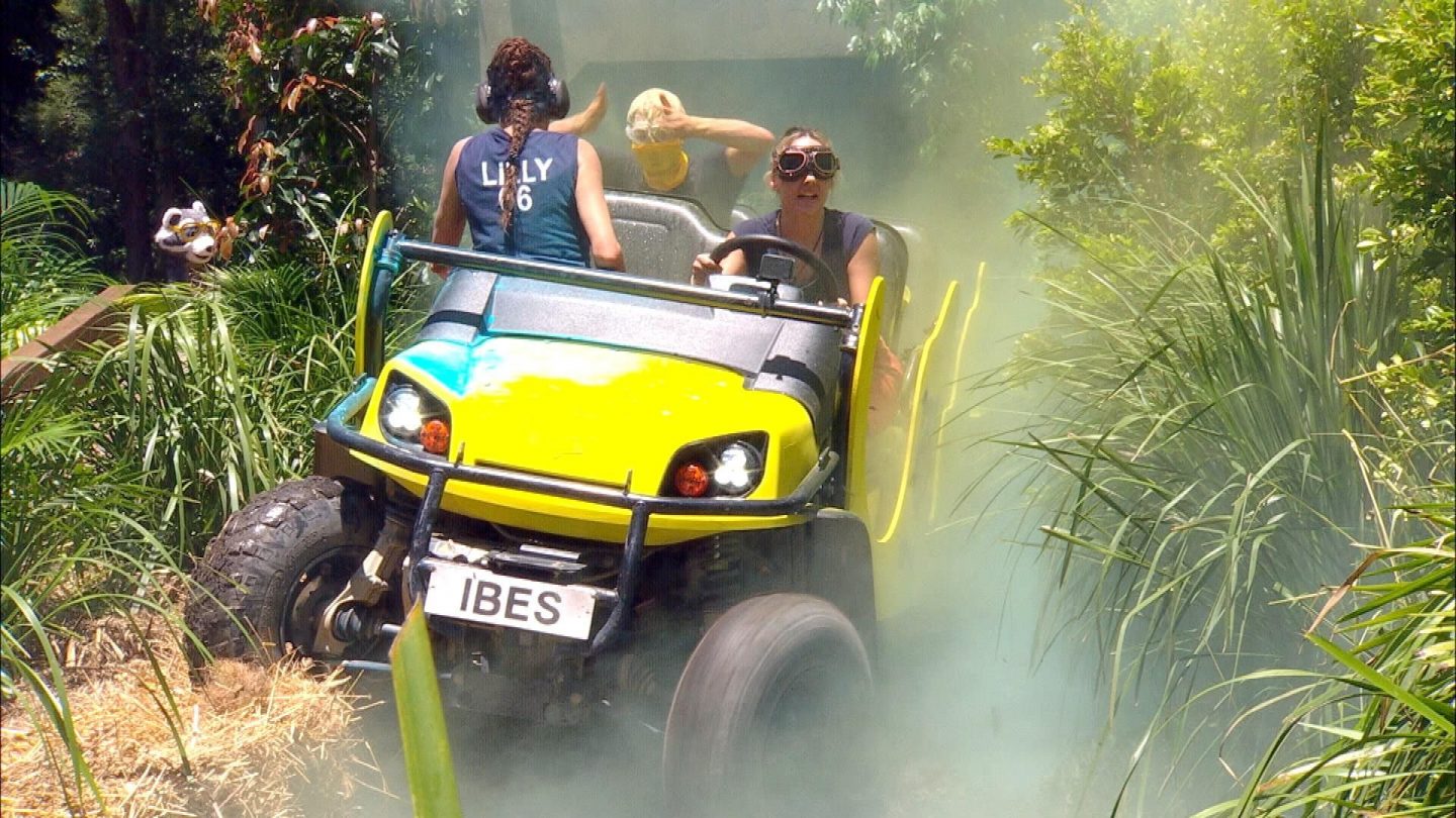 Während der Dschungelprüfung rast ein gelb-blaues Offroad-Fahrzeug mit der Aufschrift „IBES“ durch dichtes Buschwerk. Lilly Becker sitzt auf dem Beifahrersitz, während eine Mitstreiterin mit Schutzbrille am Steuer lenkt. Dichter Rauch steigt auf, während im Hintergrund eine weitere Kandidatin mit verbundenen Augen und Kopfschutz versucht, sich auf das Geschehen vorzubereiten. Die Herausforderung verspricht Tempo, Chaos und jede Menge Adrenalin.