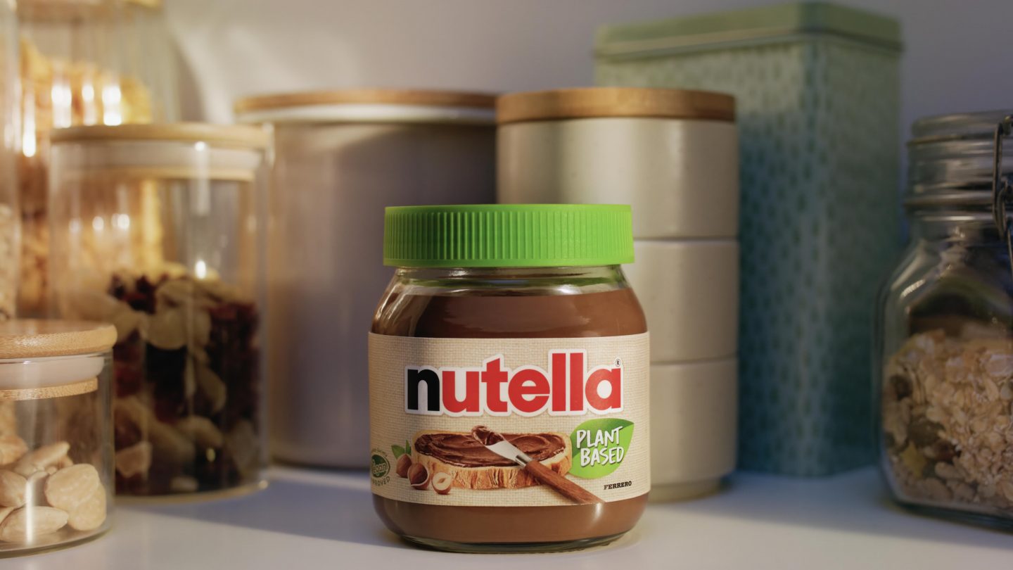 in Glas nutella Plant-Based mit grünem Deckel steht in einer Küche vor Vorratsgläsern. Das Etikett zeigt ein Stück Brot mit dem veganen Aufstrich und hebt die pflanzenbasierte Rezeptur hervor.