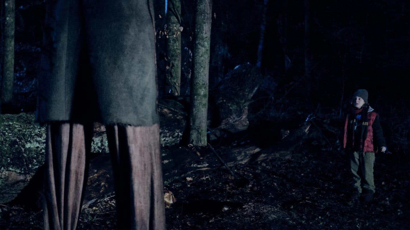 Der kleine Paul steht verängstigt im dunklen Wald vor einem unheimlichen, stelzenartigen Wesen. Die Szene ist von düsterer Atmosphäre geprägt.