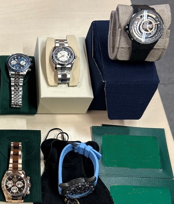 Mehrere beschlagnahmte Luxusuhren liegen auf einem Tisch. Sie sind in unterschiedlichen Designs und Farben zu sehen. Einige Uhren haben Metallarmbänder, andere Leder- oder Kunststoffarmbänder. Sie sind teils auf weichen Uhrenkissen oder in Boxen präsentiert. Diese Uhren wurden vom Zoll am Grenzübergang Konstanz-Autobahn sichergestellt, da sie illegal eingeführt werden sollten.
