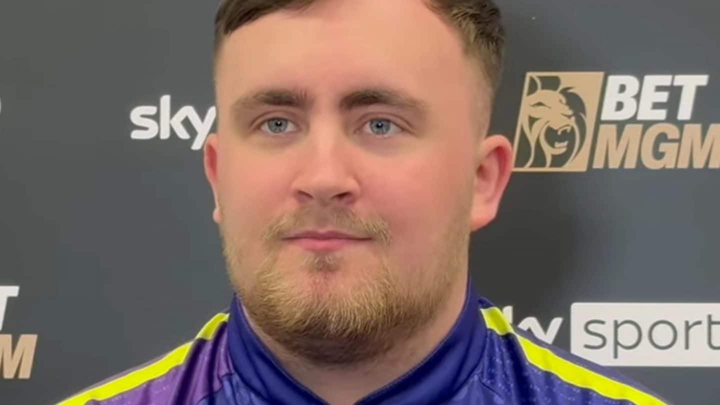 Luke Littler, Weltmeister im Dart-Sport, im offiziellen Outfit vor einer Sponsorenwand mit Logos von BetMGM und Sky Sports.