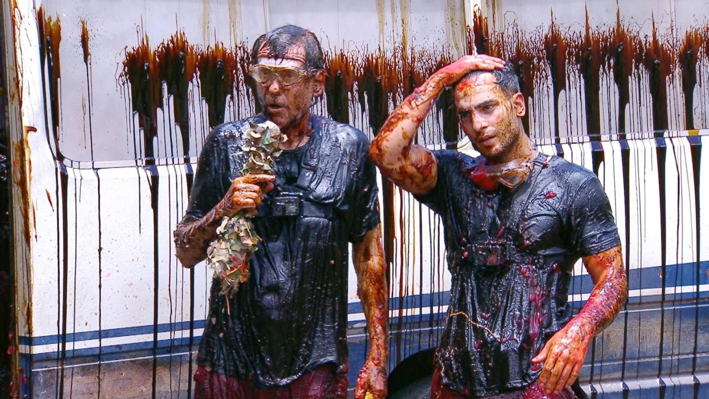 Jörg Dahlmann und Timur Ülker stehen nach der Dschungelprüfung „Bus- und Bäh-Tag“ komplett mit dunklen Flüssigkeiten und Schleim überzogen vor einem verschmutzten Bus. Beide tragen schwarze Shirts, Schutzbrillen und sehen erschöpft aus. Jörg hält Eukalyptusblätter in der Hand, Timur wischt sich mit der Hand durch die Haare.