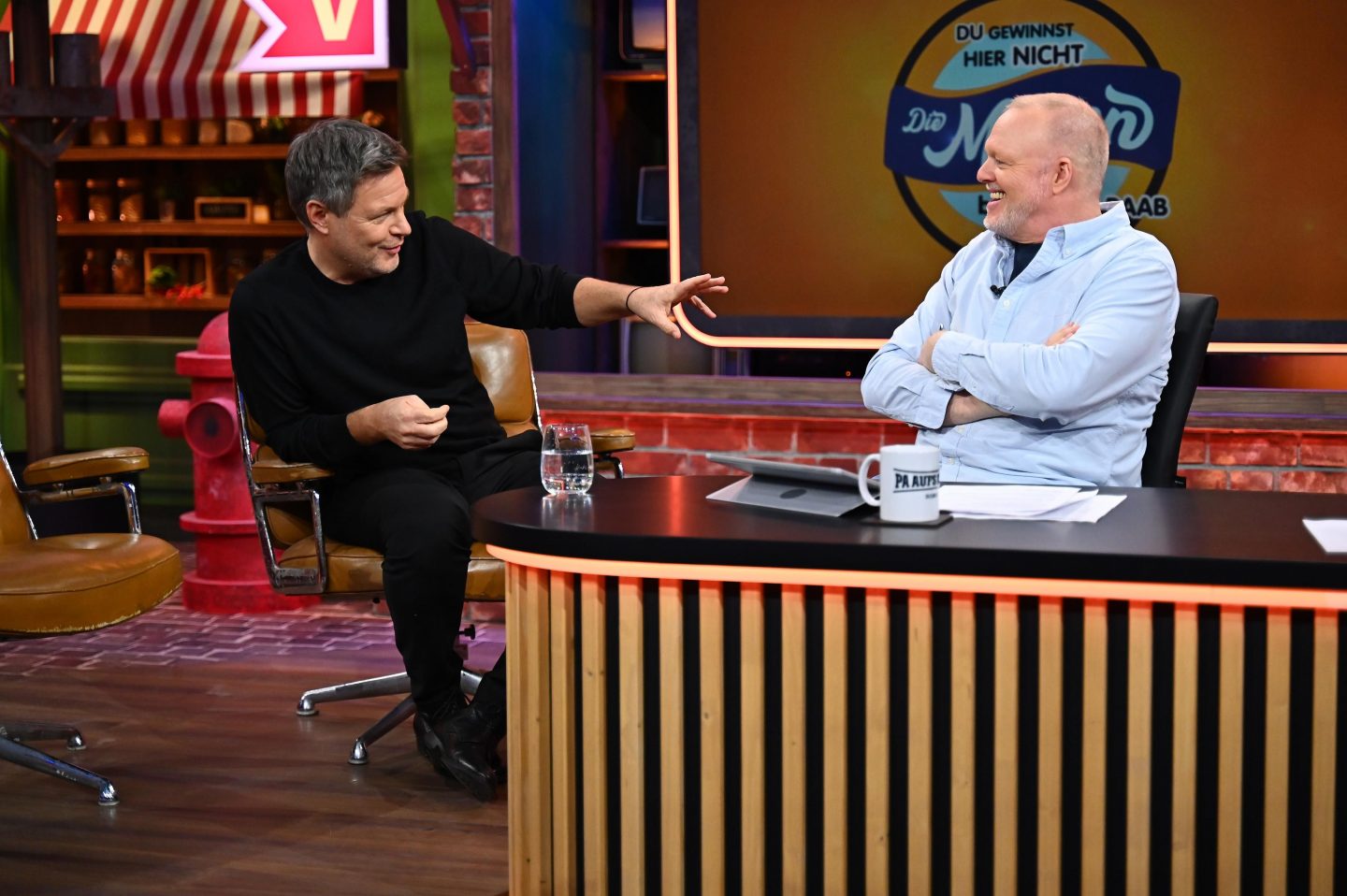Robert Habeck und Stefan Raab im Gespräch in der Show Du gewinnst hier nicht die Million bei Stefan Raab. Habeck gestikuliert, während Raab mit verschränkten Armen lacht. Im Hintergrund das Show-Logo.