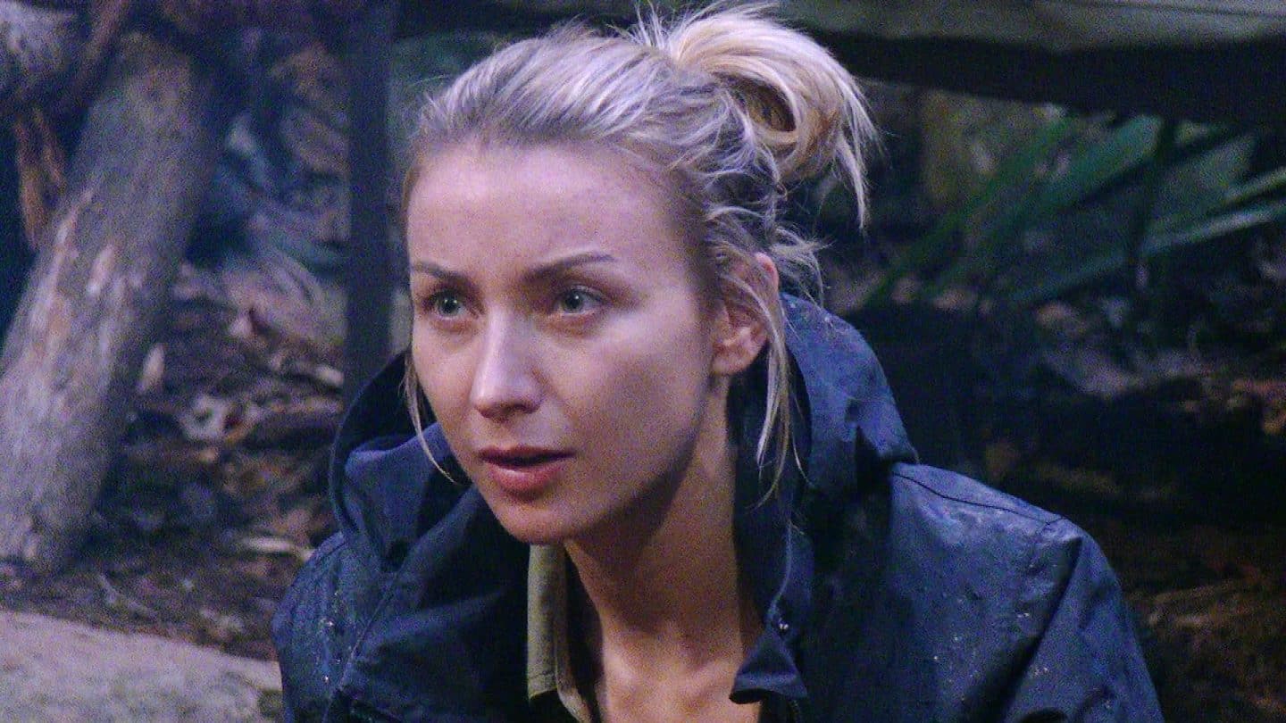 Anna-Carina Woitschack sitzt mit fassungslosem Blick im Dschungelcamp, sichtlich überrascht von Timurs Vorwurf. Ihr blonder Zopf ist locker gebunden, sie trägt eine dunkle Regenjacke, während ihre Mimik Verwunderung und Unverständnis ausdrückt. Der Hintergrund zeigt das Camp-Setting mit Holzstämmen und Pflanzen, die angespannte Stimmung ist deutlich spürbar.






