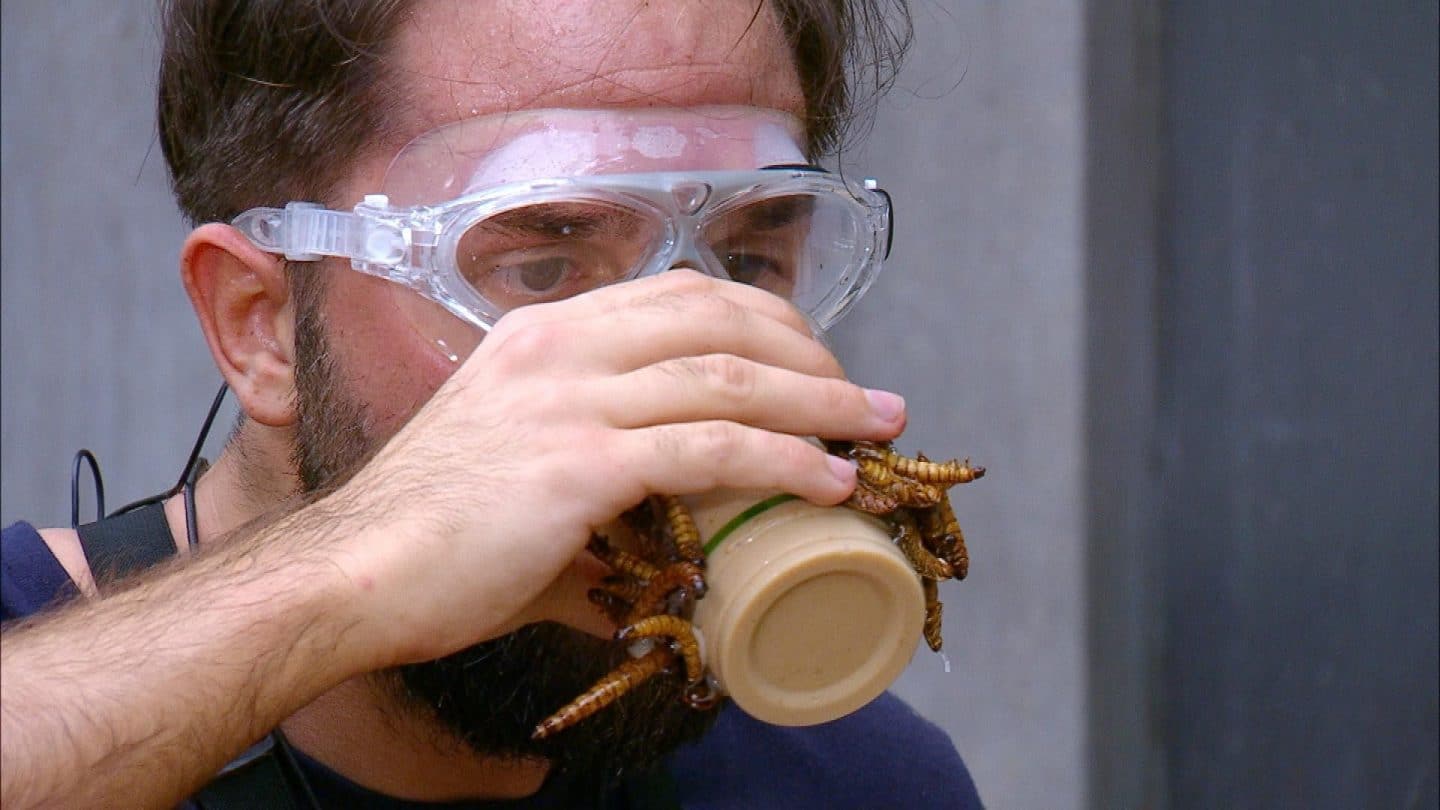 Maurice Dziwak trägt eine Schutzbrille und trinkt einen braunen Shake während der Dschungelprüfung „Einkaufs-Strafe“. Mehrere große Mehlwürmer und Kakerlaken krabbeln über seine Hand und das Glas. Er schaut konzentriert und fokussiert, während er die eklige Spezialität bei „Gyros Antony“ zu sich nimmt.







