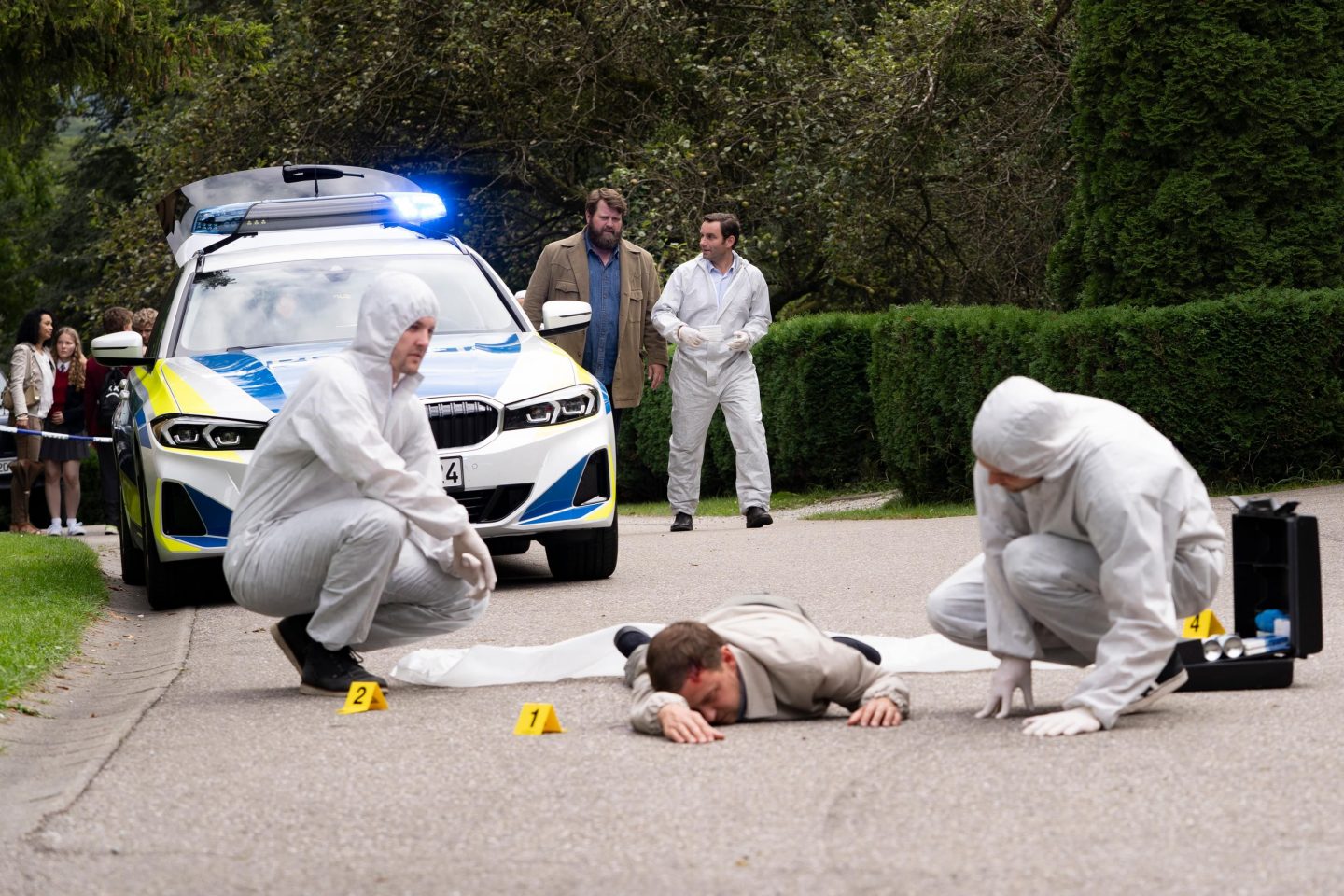 V.l.: Kommissar Behringer (Antoine Monot), Vertrauenslehrer/Mordopfer Chris Dammers (Felix von Bredow) und Sebastian Loncar (Jonas Laux). Basti führt Behringer zum Tatort vor der Hoffmann-von-Fallersleben-Privatschule. Die Leiche des Vertrauenslehrers Chris Dammers wird von Mitarbeitern der Spurensicherung begutchatet.