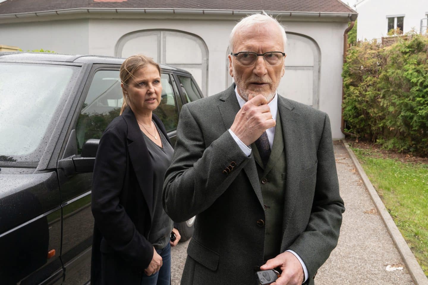 "Die Chefin - Murnau": Dr. Jakob Murnau (Ernst Stötzner) steht nachdenklich in der Auffahrt vor seinem schwarzen SUV. Hinter ihm steht Vera Lanz (Katharina Böhm), die ihn kritisch betrachtet.

