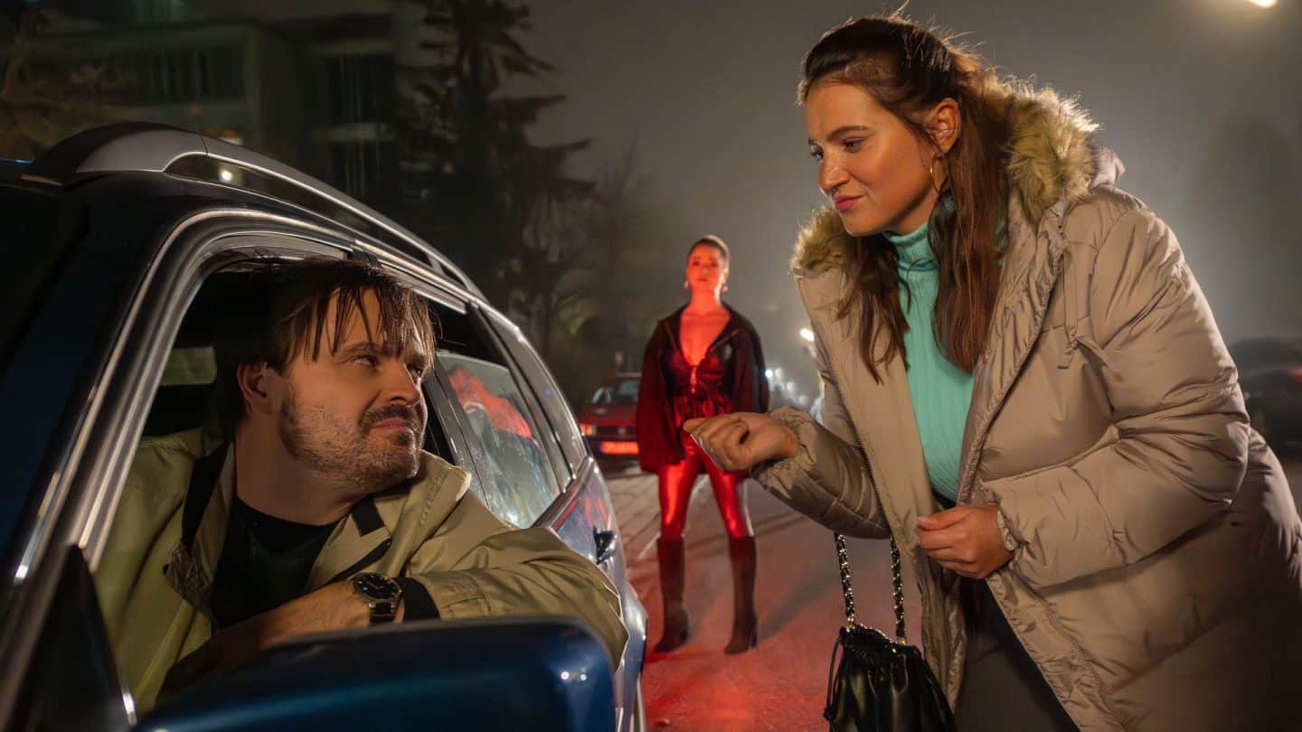 "Aktenzeichen XY... Cold Cases": Nachgestellte Szene. Es ist Nacht. Ein Autofahrer schaut mit angelehntem Arm vom Fenster aus zu einer Frau die neben dem Auto steht. Beide schauen sich intensiv in die Augen. Hinter ihnen steht eine leicht bekleidete junge Frau und schaut sie an.
