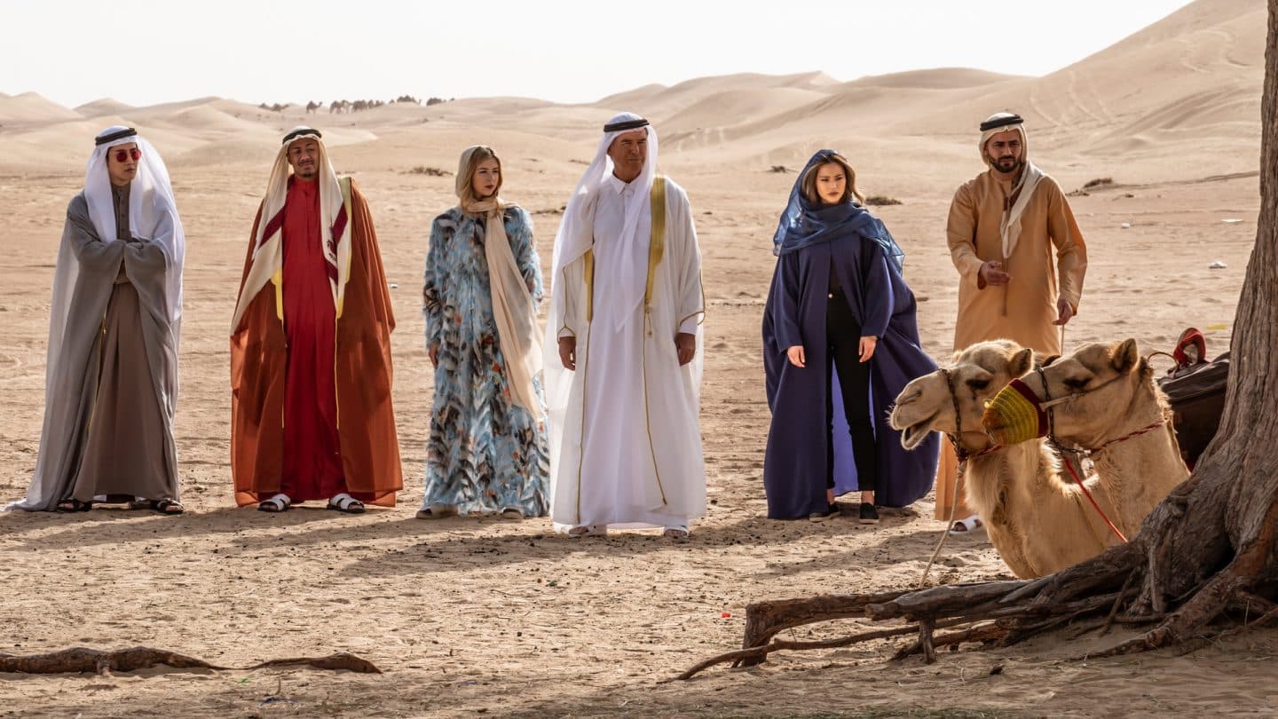 "The Misfits - Die Meisterdiebe": Die Misfits Wick (Mike Angelo), Ringo (Nick Cannon), Hope (Hermione Corfield), Richard (Pierce Brosnan), Violet (Jamie Chung) und The Prince (Rami Jaber) stehen in der Wüste. Im Vordergrund sieht man hinter einem Baum zwei Dromedare sitzen.
