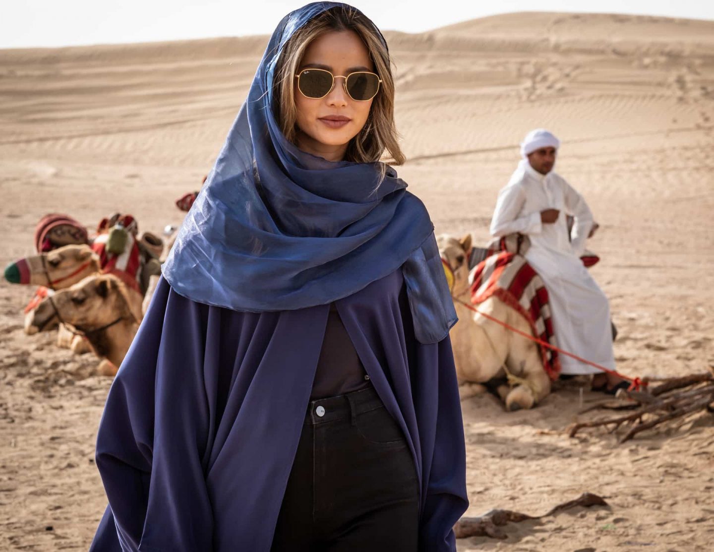 "The Misfits - Die Meisterdiebe": Hope (Hermione Corfield) trägt einen Kaftan und Sonnenbrille. Im Hintergrund seiht man einen Einheimischen und Dromedare.
