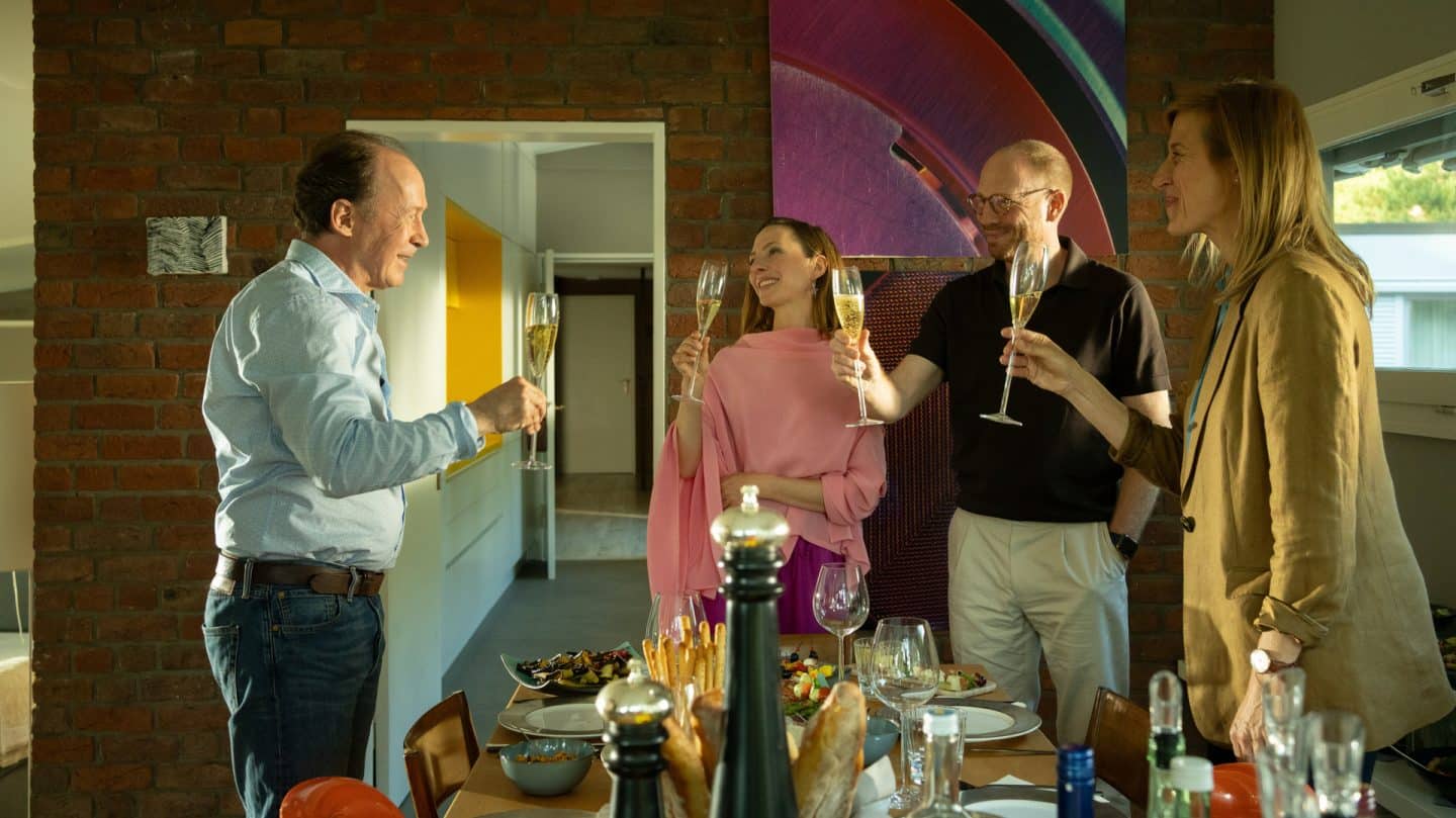 "Wendland - Stiller und der Teufelssauger": Jakob Stiller (Ulrich Noethen), Oda Nolde (Katharina Schüttler), Jan Nolde (Johann von Bülow) und Silke Landauer (Helene Grass) stehen an einem gedeckten Tisch und stoßen mit Sekt an.

