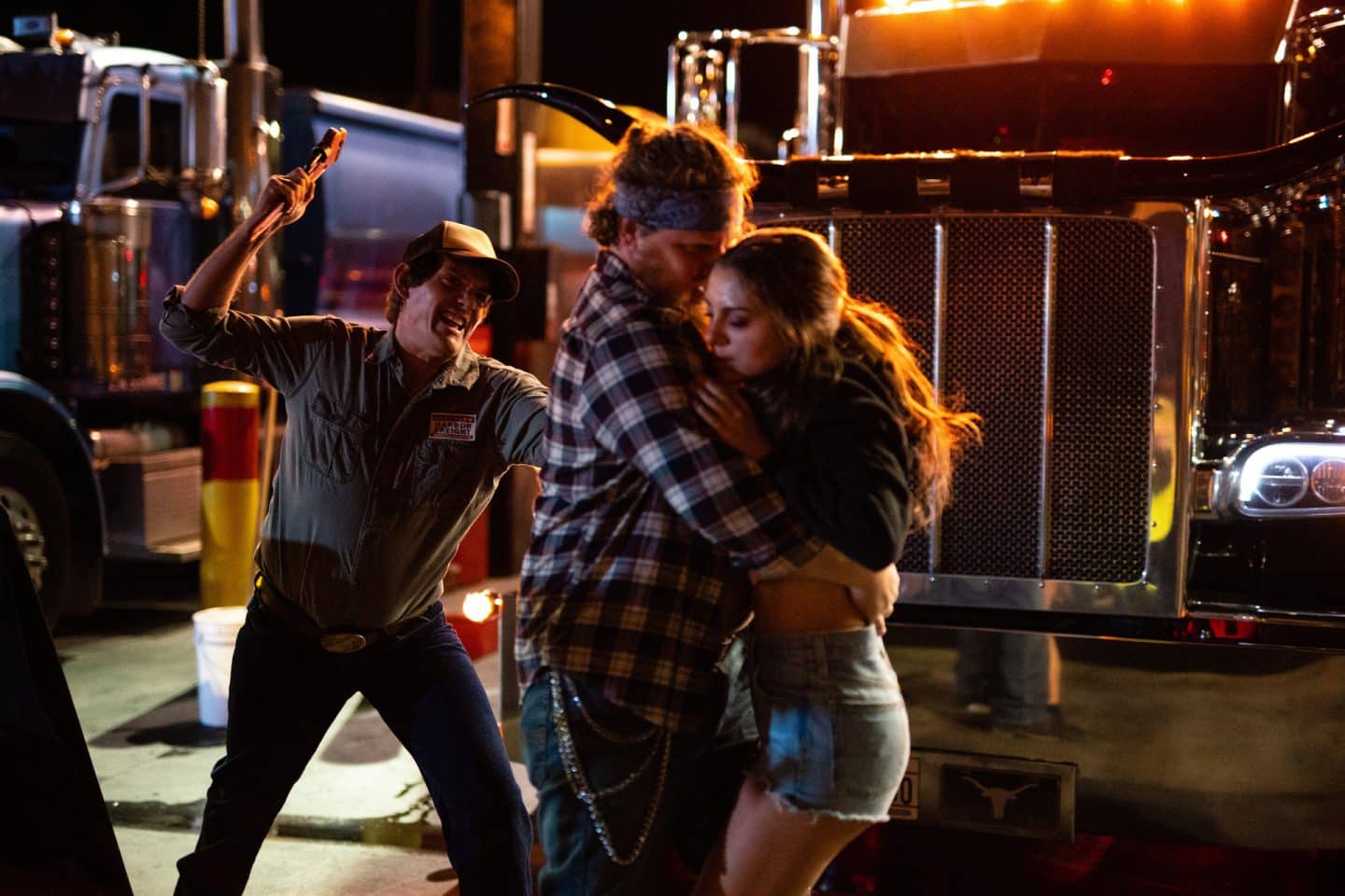 "Die Spur des Killers – Midnight in the Switchgrass": Vor abgestellten Trucks auf einem nächtlichen Parkplatz reißt ein unbekannter Mann (Komparse) in Jeans und kariertem Hemd Tracy (Caitlin Carmichael) an sich, während Peter (Lukas Haas) ihn von hinten mit einem Hammer attackiert.