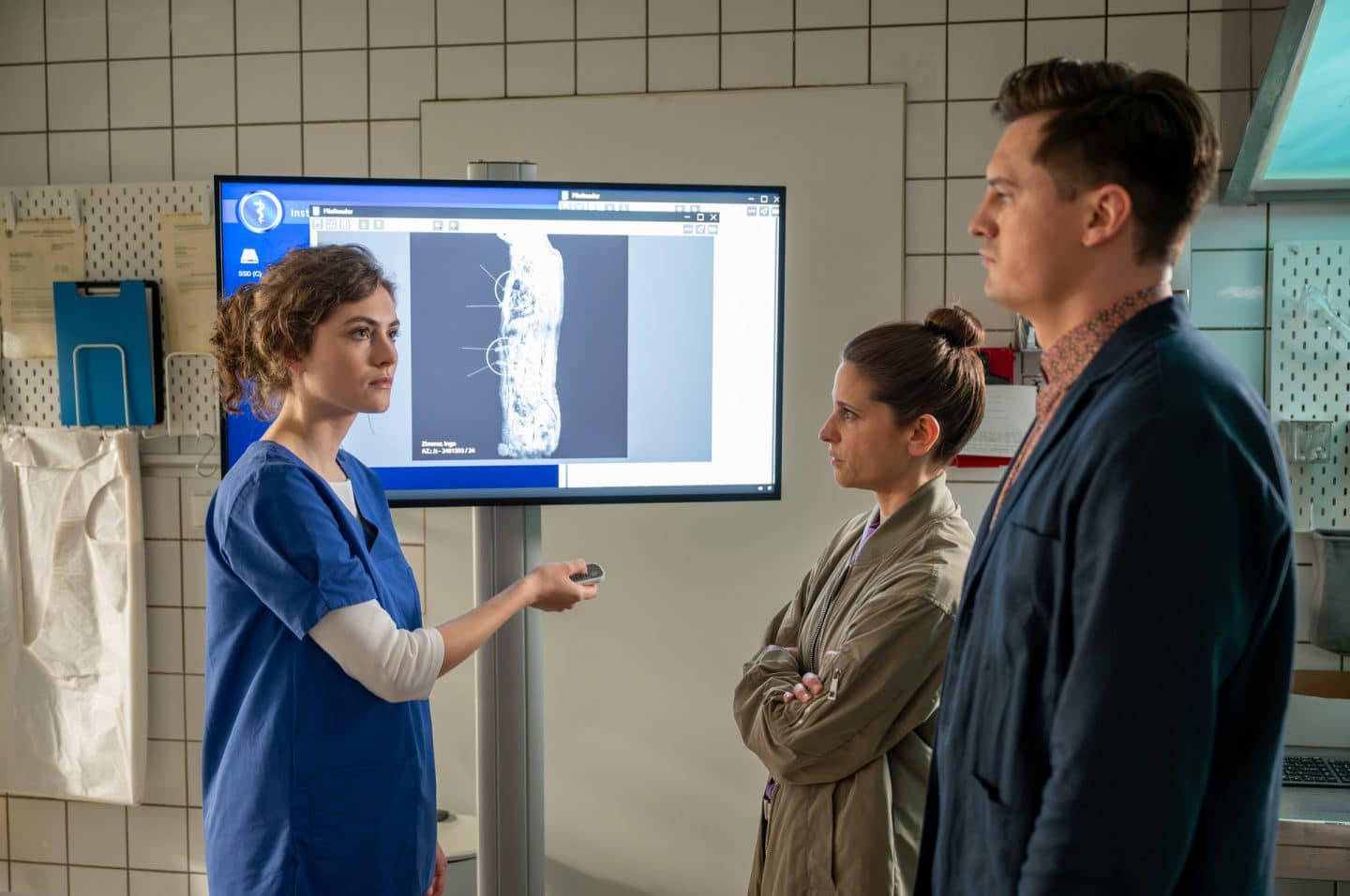 "Der Staatsanwalt - Zu allem entschlossen": Julia Schröder (Anika Baumann) und Alexander Witte (Jannik Mioducki) stehen Lili Pohl (Luise Ehl) in einem Raum der Rechtsmedizin gegenüber. Pohl hält eine Fernbedienung in ihrer rechten Hand, auf dem Bildschirm hinter ihr ist ein Röntgenbild zu sehen.
