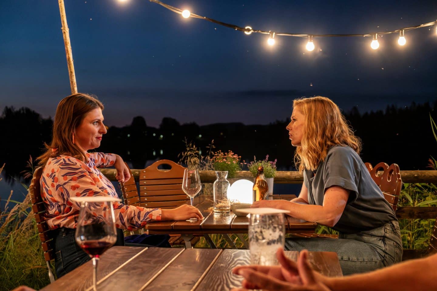 "Marie fängt Feuer - Vergeben und Vergessen": Marie (Christine Eixenberger) sitzt mir ihrer Kollegin Toni (Lisa Jopt) an einem Tisch in einem Biergarten. Es stehen Getränke auf dem Tisch und sie unterhalten sich. Es dämmert schon, die Lichter sind schon an.