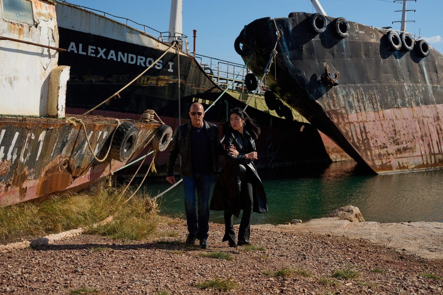 "Yvonne und der Tod": Tim Koller (Moritz Führmann) steht vor einem Tisch auf einem Autobahnrastplatz. Er hat einen Koffer vor sich abgestellt und hantiert damit. Neben ihm betrachtet Conny Roth (Sina Bianca Hentschel) den Inhalt des Koffers.
