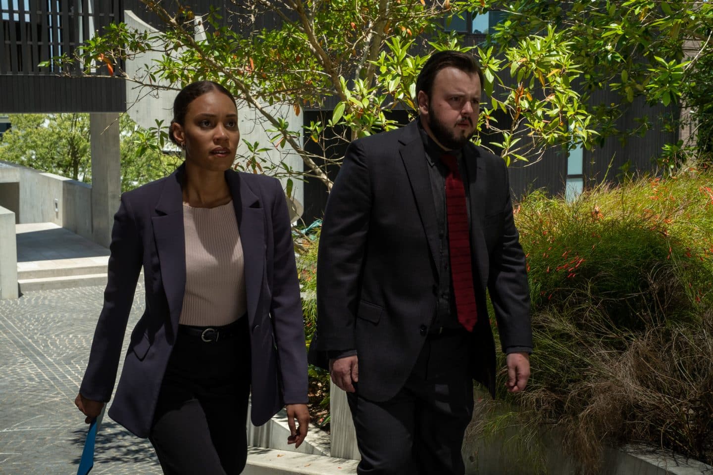 "North Shore – Tod in Sydney – Sophies Laptop": DS Meg Driscoll (Kirsty Sturgess) und DS Max Drummond (John Bradley) gehen nebeneinander durch ein Wohngebiet. Meg trägt eine blaue Dokumentenmappe.
