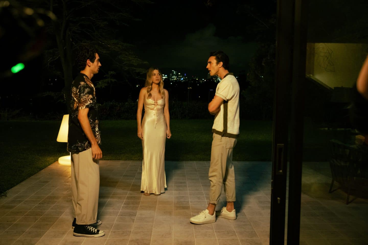 "North Shore – Tod in Sydney – Die Spur des Blutes": Oscar (Jonathan Lagudi) und Tom (Max Mayer-Rayment) stehen sich bei Nacht auf einer Terrasse gegenüber. Tom wirkt wütend. Etwas im Hintergrund steht Sophie (Bailey Spalding) und beobachtet die beiden.