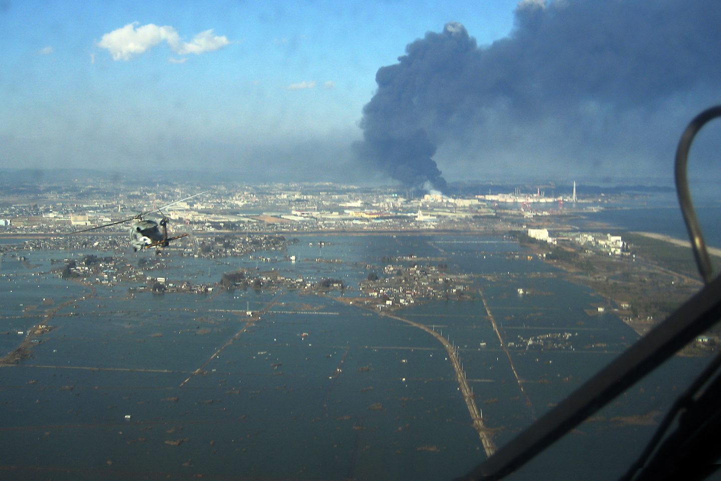 Luftaufnahme des Sendai-Hafens mit Blick auf überflutetes Gebiet und Brände (12. März 2011)
