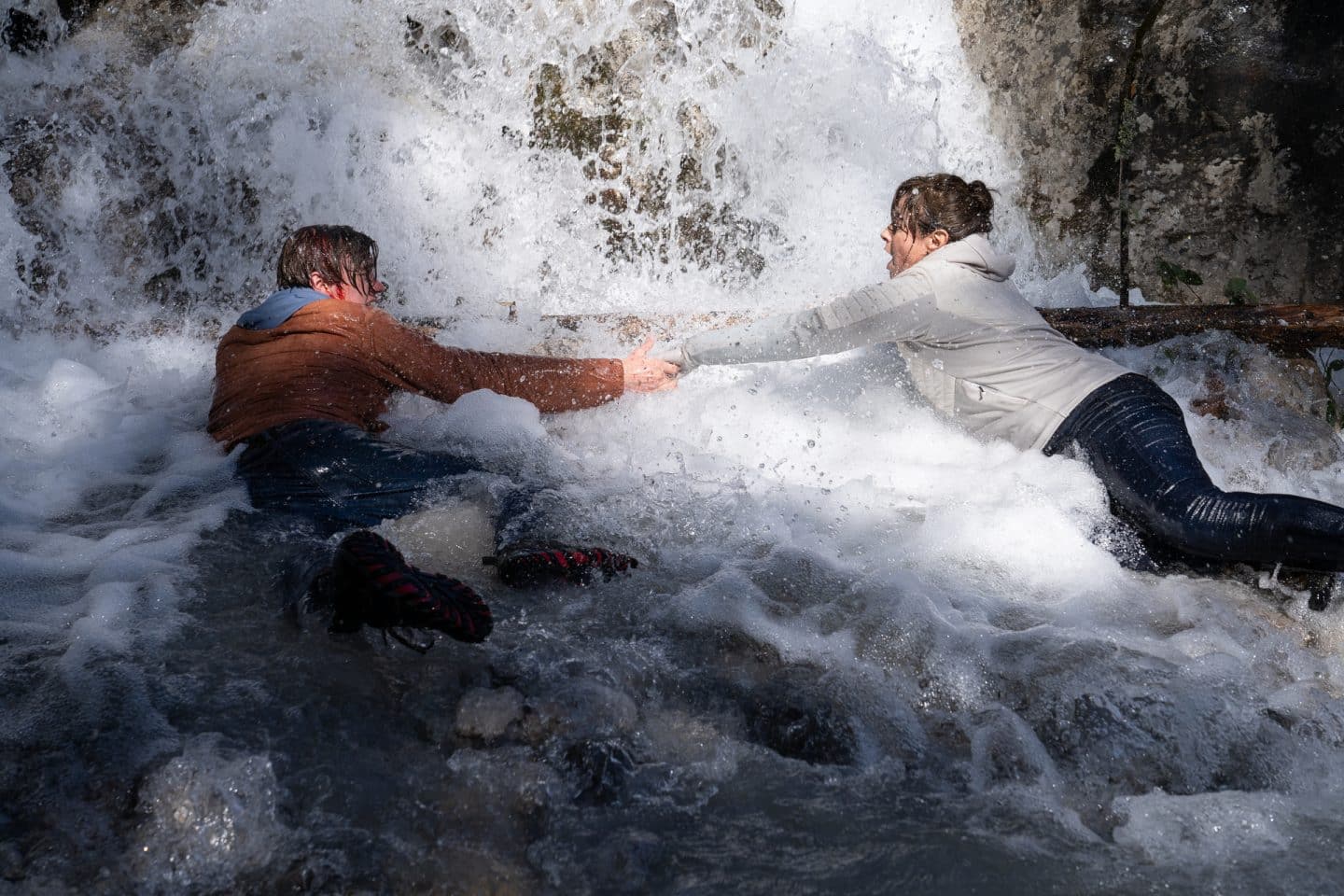"Die Bergretter: Im Gipfelbuch": Felix (Alessandro Schuster) und Luisa Hertinger (Carolina Vera) liegen im Wasser unter einem Wasserfall und halten sich angestrengt an der Hand fest. Felix blutet am Kopf.
