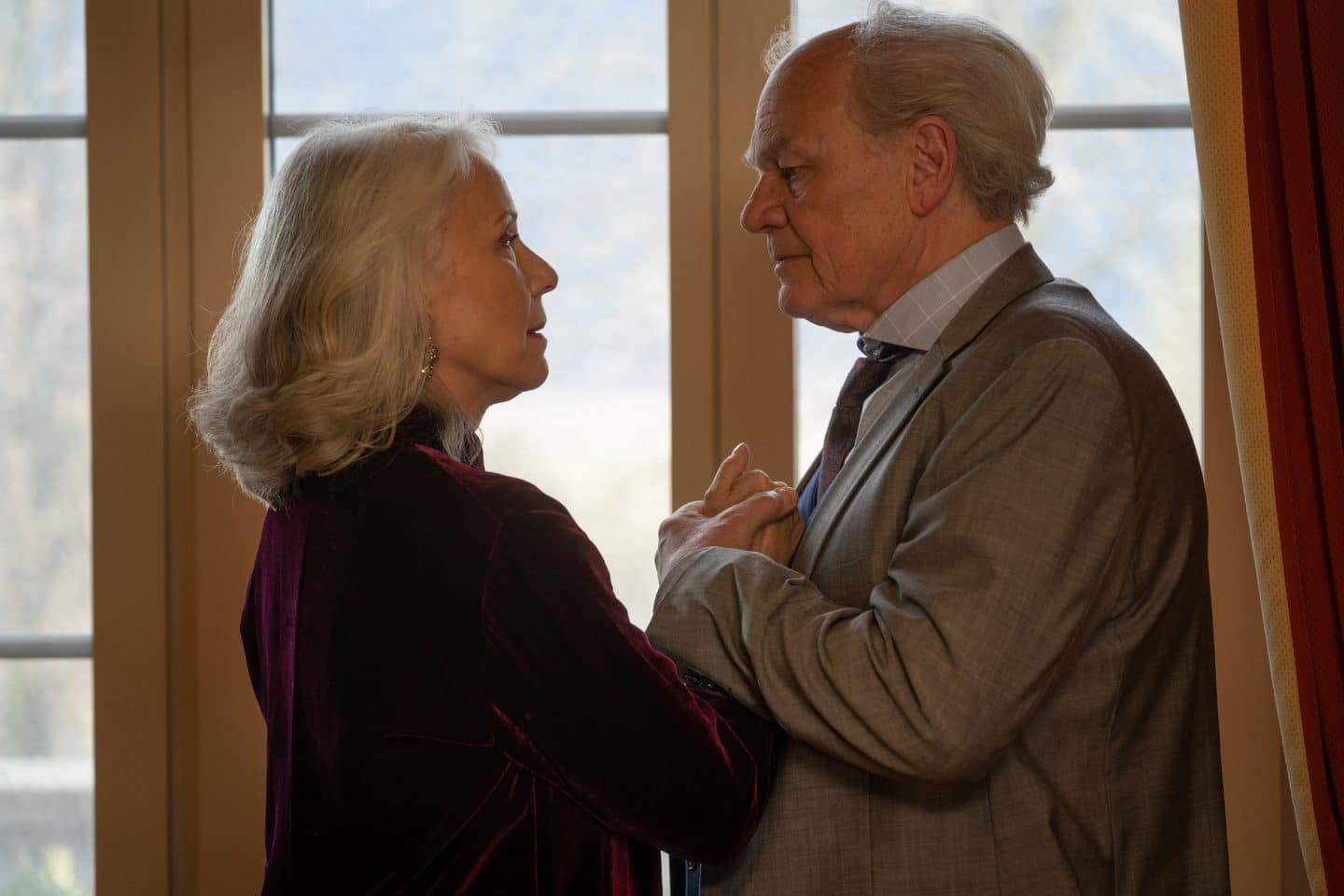 "Die Bergretter: Eiskalte Wahrheit (2)": Johanna (Michaela Rosen) und Peter (Michael König) stehen mit verschlungenen Händen vor der Brust am Fenster und blicken sich an.
