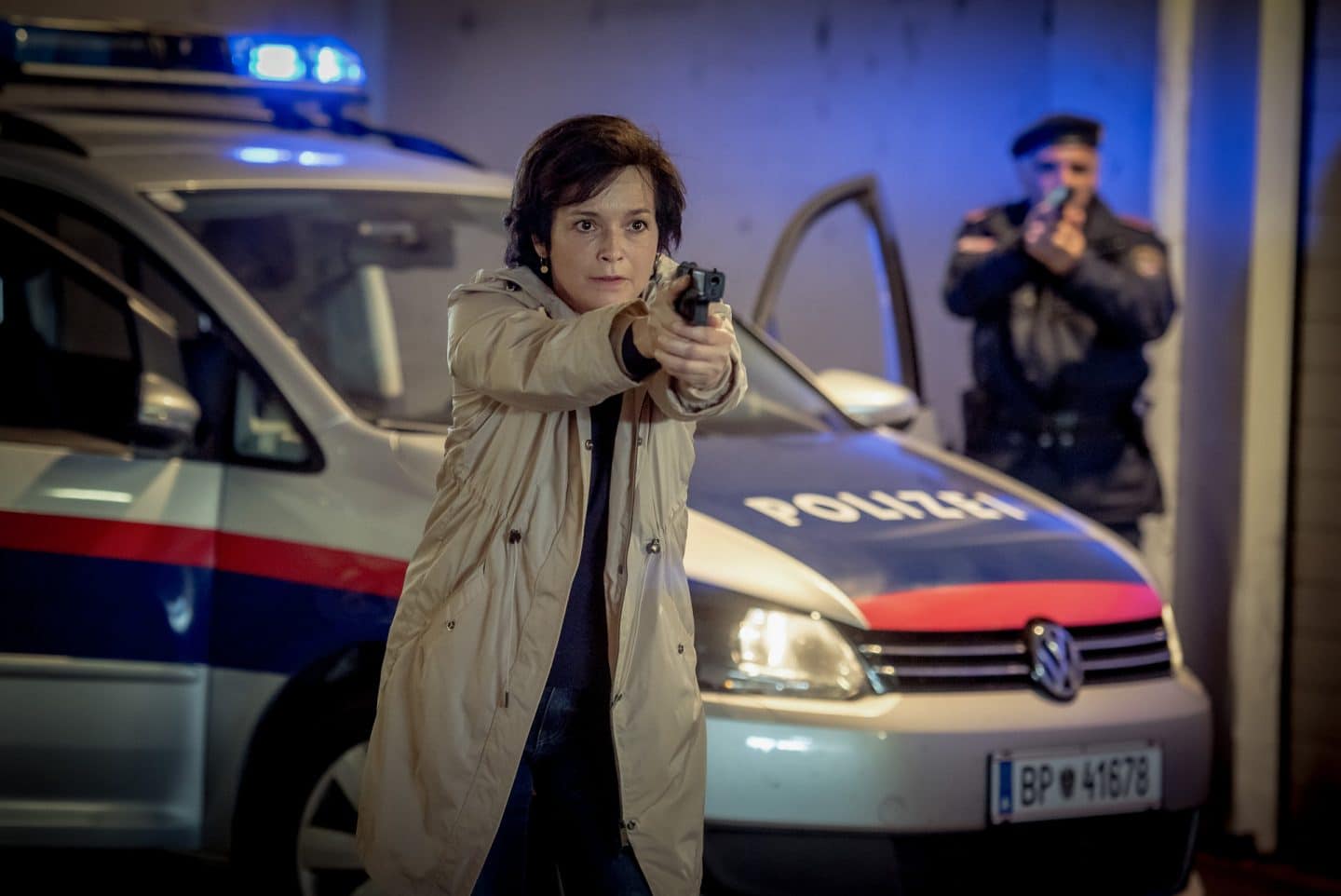 "SOKO Linz - Wir kennen dich": Johanna "Joe" Haizinger (Katharina Stemberger) steht mit einer gezogenen Waffe im Anschlag vor einem Polizeiauto. Sie sieht sehr entschlossen aus. Hinter dem Wagen seitlich sieht man einen weiteren Polizeibeamten mit Waffe im Anschlag stehen.