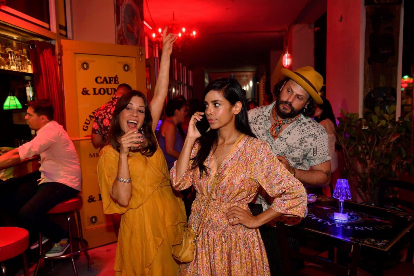 "Das Traumschiff: Miami": In einer kubanischen Bar am Abend, bei gedämmten Licht: Genervt blickend telefoniert Dr. Jessica Delgado (Collien Ulmen-Fernandes) mit dem Handy. Ihre Freundin Maike Kappes (Birthe Wolter) tanzt ausgelassen neben ihr, während sie ein Glas in den Händen hält. Im Hintergrund steht Matteo Diaz (Manuel Cortez) und beobachtet die beiden aufmerksam.