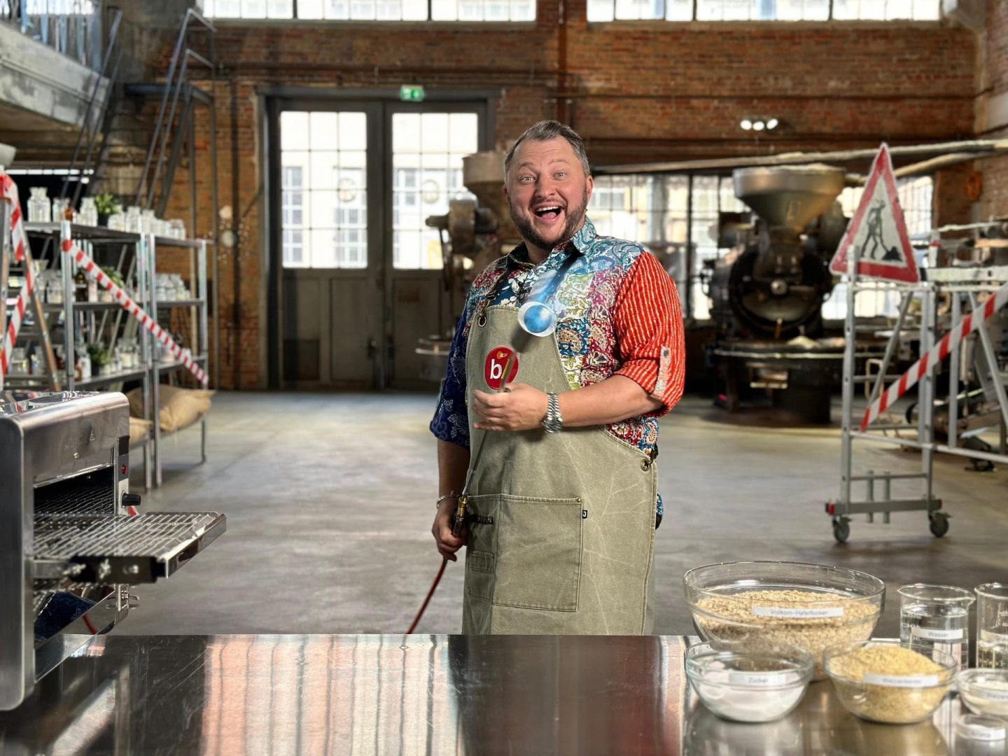 "besseresser: Die Tricks von Ehrmann, Dr. Oetker & Co. - Sebastian Lege deckt auf": Sebastian Lege steht mit einem großen Bunsenbrenner in der Werkstattküche.