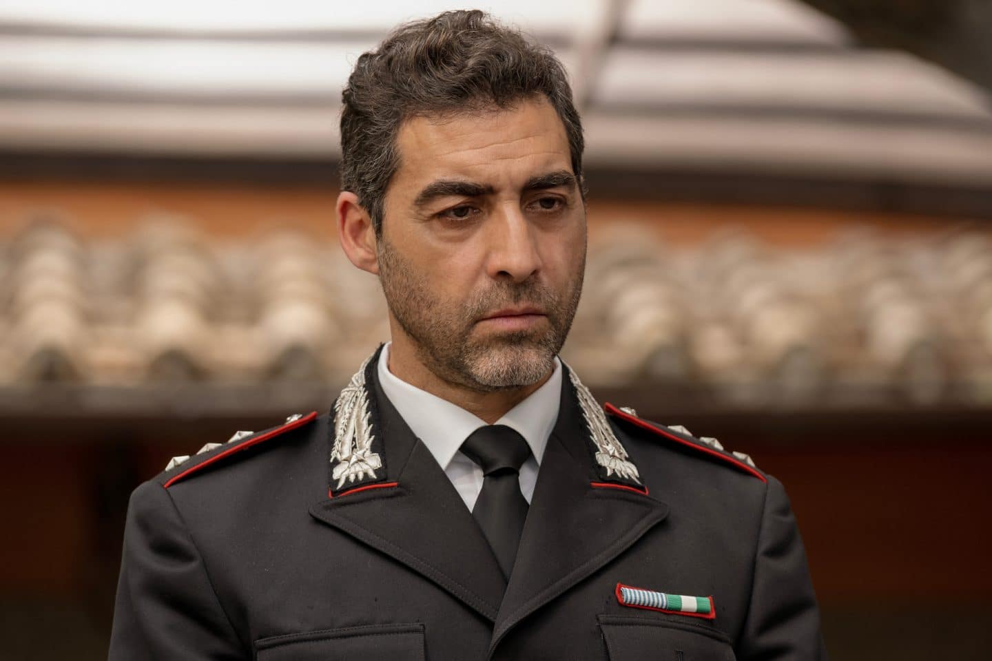 "Signora Volpe - Verstrickung": Capitano Giovanni Riva (Giovanni Cirfiera) steht in Uniform vor einem Gebäude, das im Hintergrund unscharf zu sehen ist.
