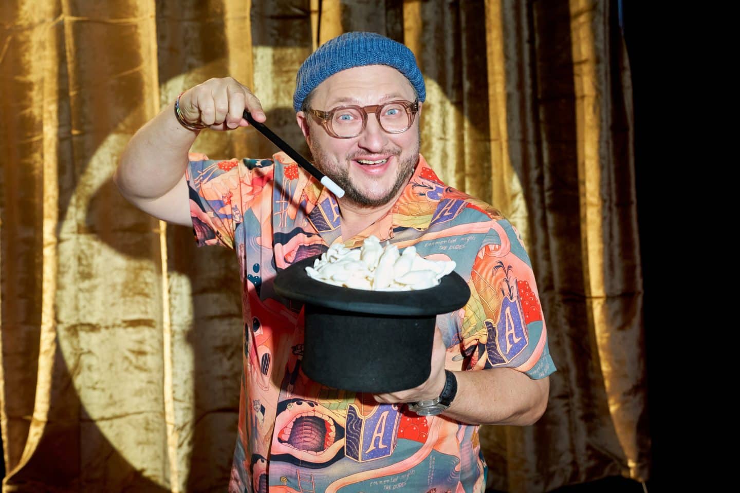 "besseresser: Die Tricks von Haribo, Intersnack & Co.": Sebastian Lege steht vor einem goldenen Theatervorhang, er hält einen schwarzen Zylinder in der Hand, in dem Weiße Mäuse aus Schaumgummi stecken - er deutet mit einem Zauberstab auf den Zylinder.
