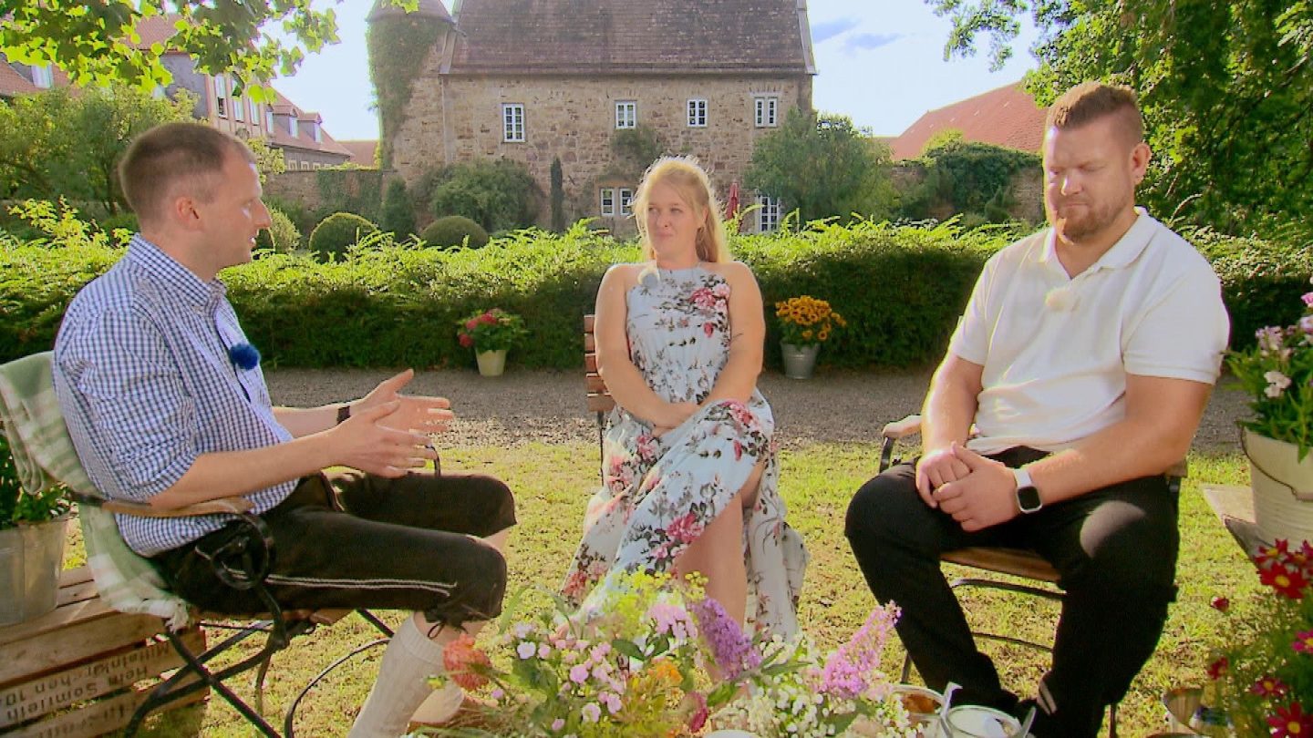 Daniel, Insa und Christoph sitzen bei „Bauer sucht Frau“ 2025 im Garten eines Bauernhofs. Insa sitzt zwischen den beiden Männern, während Daniel spricht und Christoph nachdenklich schaut – die Spannung ist deutlich spürbar.